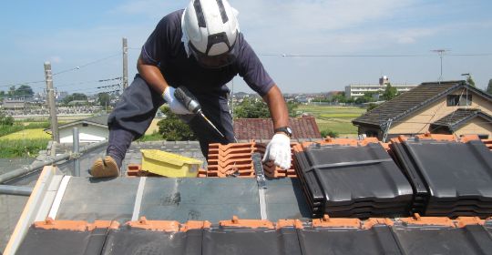 職人が屋根瓦を交換している葺き替え工事の様子